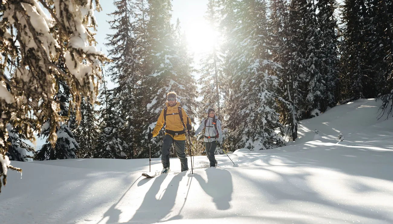 Zwei Personen beim Schneeschuhwandern durch verschneiten Wald im hellen Winterlicht