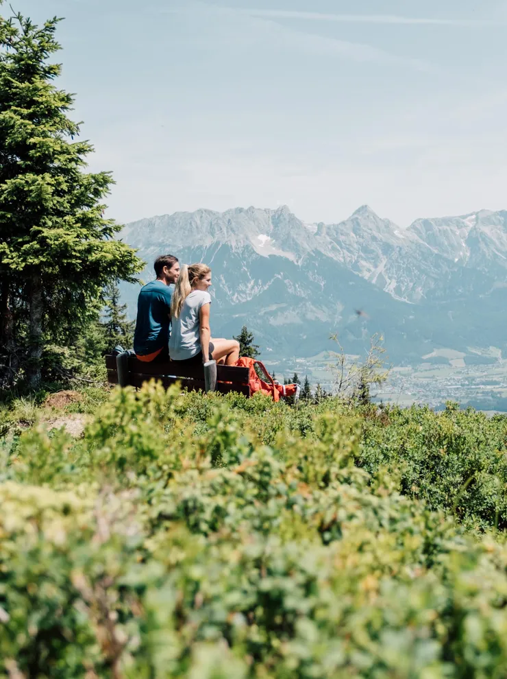 Paar sitzt auf Bergbank und genießt alpine Landschaft mit Panoramablick ins Tal