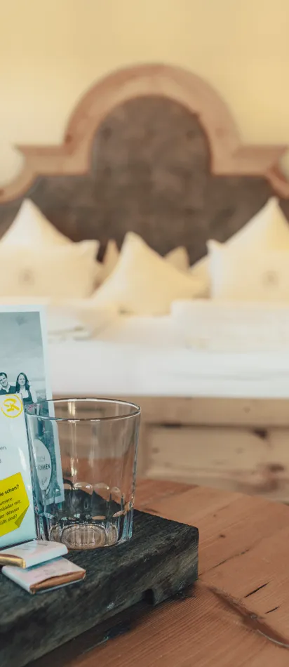 Wooden hotel room with bed, water carafe, glasses and info card on rustic table