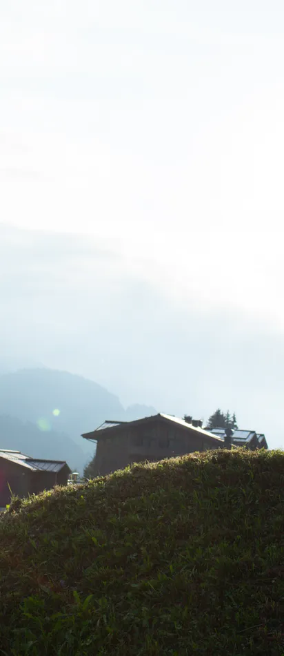Mountainbiker fährt bergauf bei Sonnenuntergang mit Alpen-Dorf und Bergen im Hintergrund