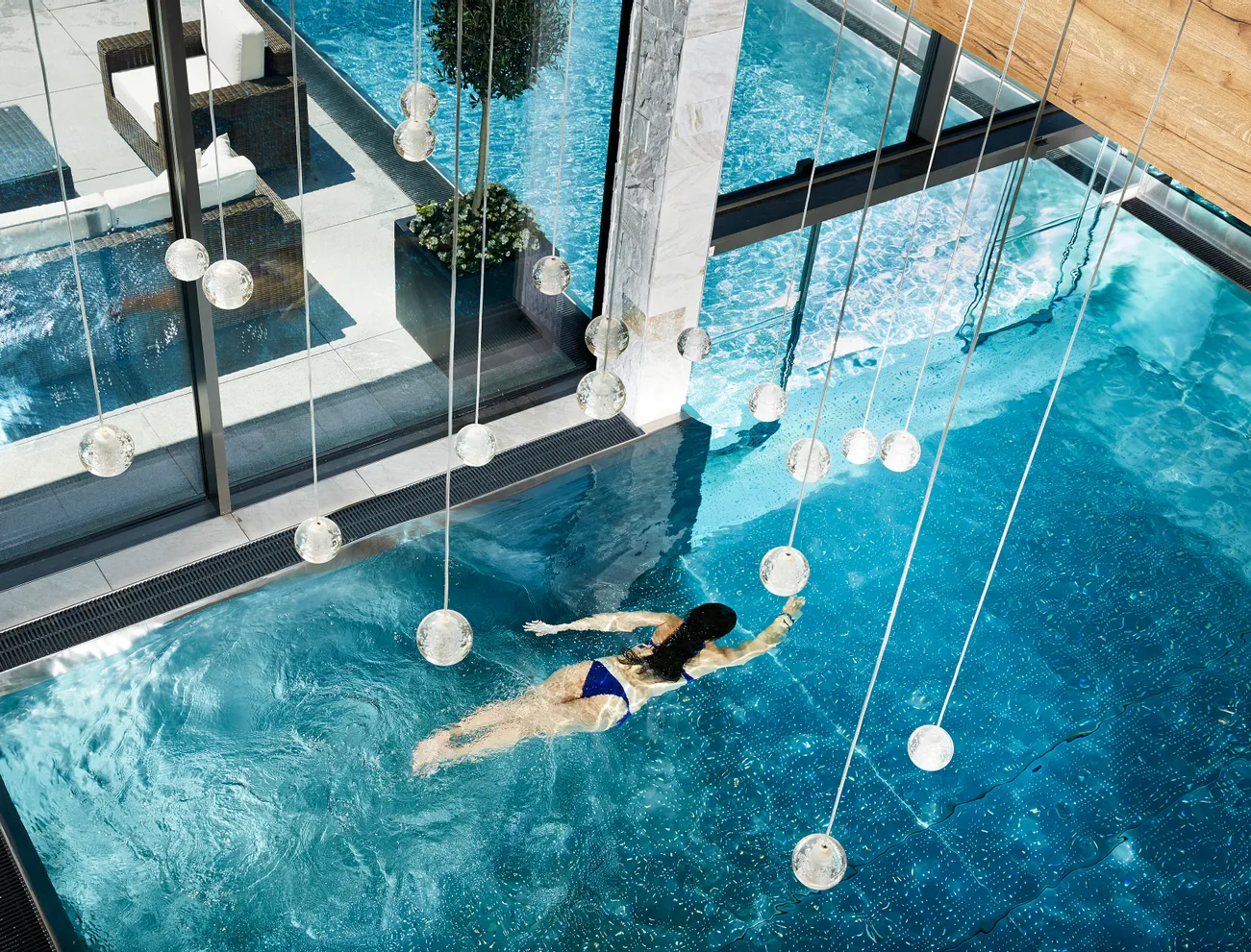 Woman swimming in luxury indoor-outdoor pool with glass walls and hanging lights