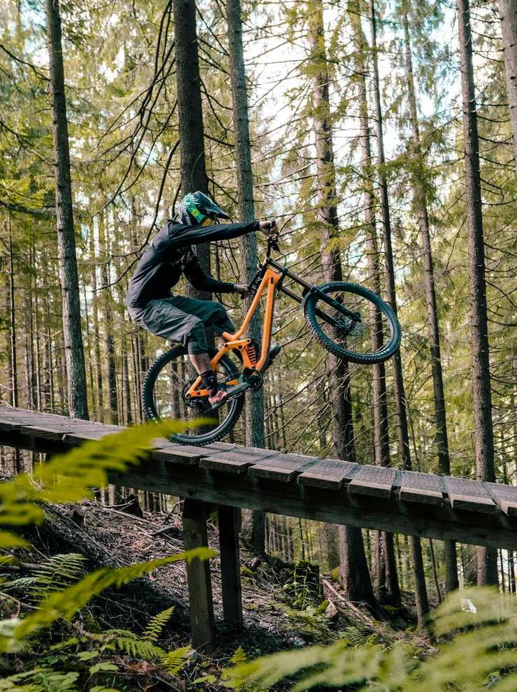 Mountainbiker macht ein Wheelie auf Holzrampe im Wald