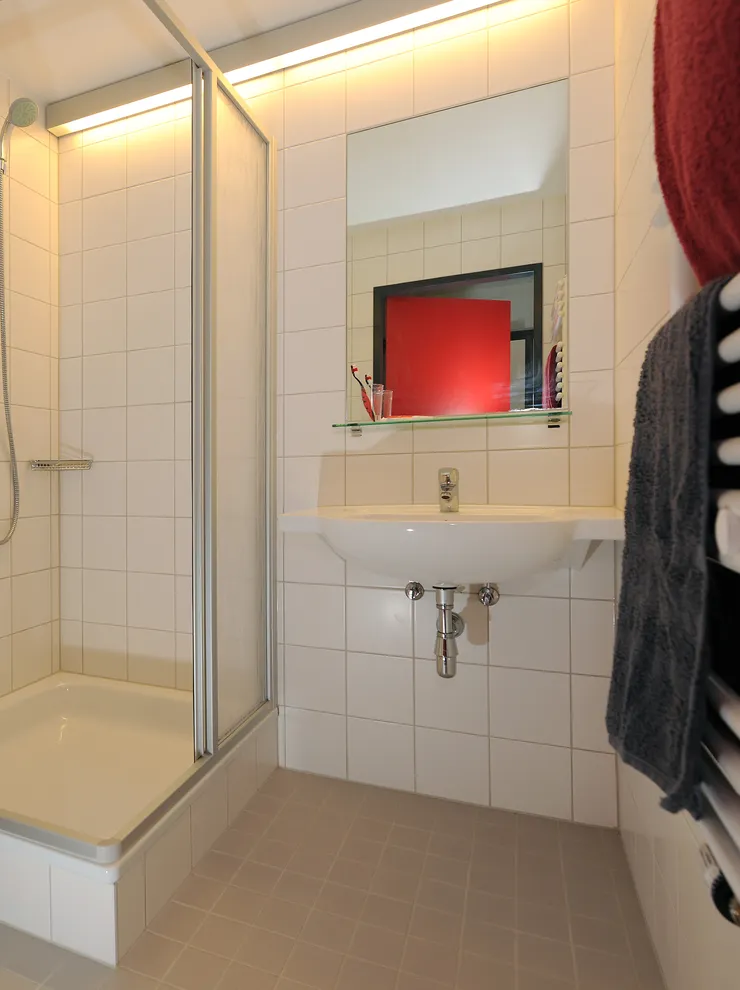 Modern bathroom with shower cabin, wall-mounted toilet, sink, and heated towel rack