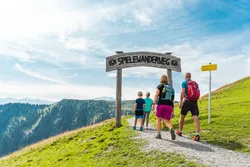 Familie wandert auf dem Spielewanderweg in den Alpen bei sonnigem Wetter