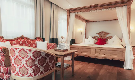 Cozy hotel room with wooden canopy bed and red baroque sofa