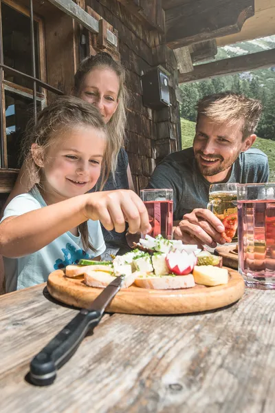 Familie nyder traditionel alpesnack ved træbord udenfor bjælkehytte