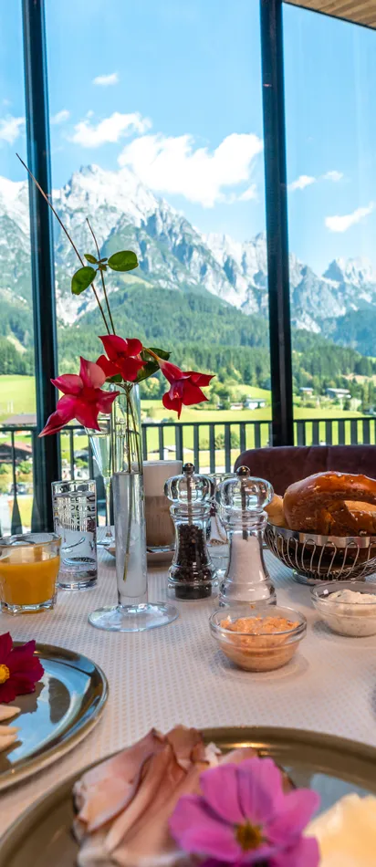 Luxuriöses Frühstück mit Gebäck, Obst und Schinken vor Bergpanorama in einem Alpenhotel