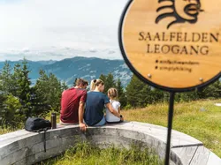 Family sitting on wooden bench overlooking mountains in Saalfelden Leogang during hike