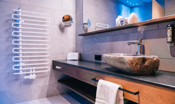 Modern bathroom with stone sink, towel heater, and wall-mounted mirror