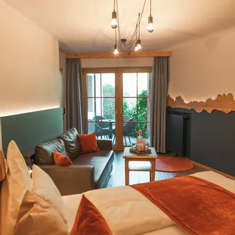 Cozy hotel room with double bed, sofa, and access to terrace with garden view