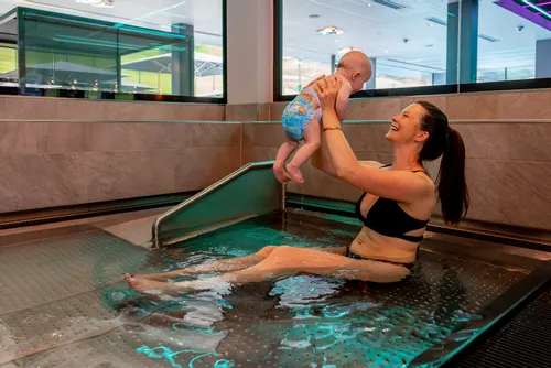 Lächelnde Mutter im Bikini hebt Baby in Schwimmwindel in einem Innenpool