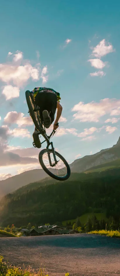 Mountainbiker springt bei Sonnenuntergang vor alpiner Landschaft