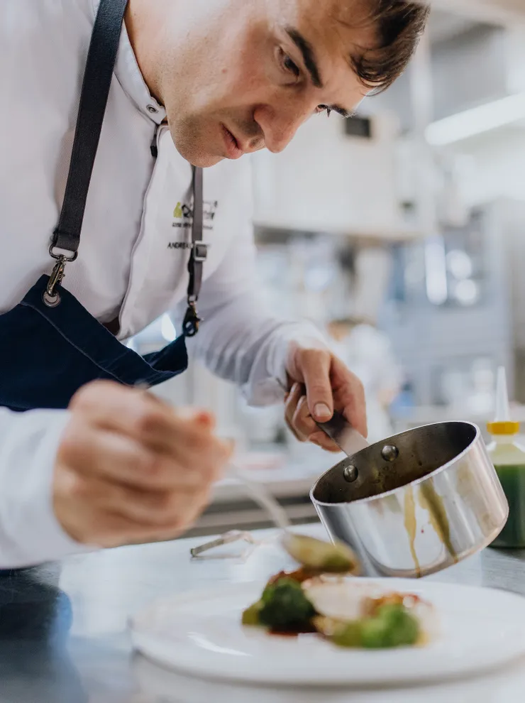 Chef in professional kitchen plating gourmet dish with sauce from saucepan