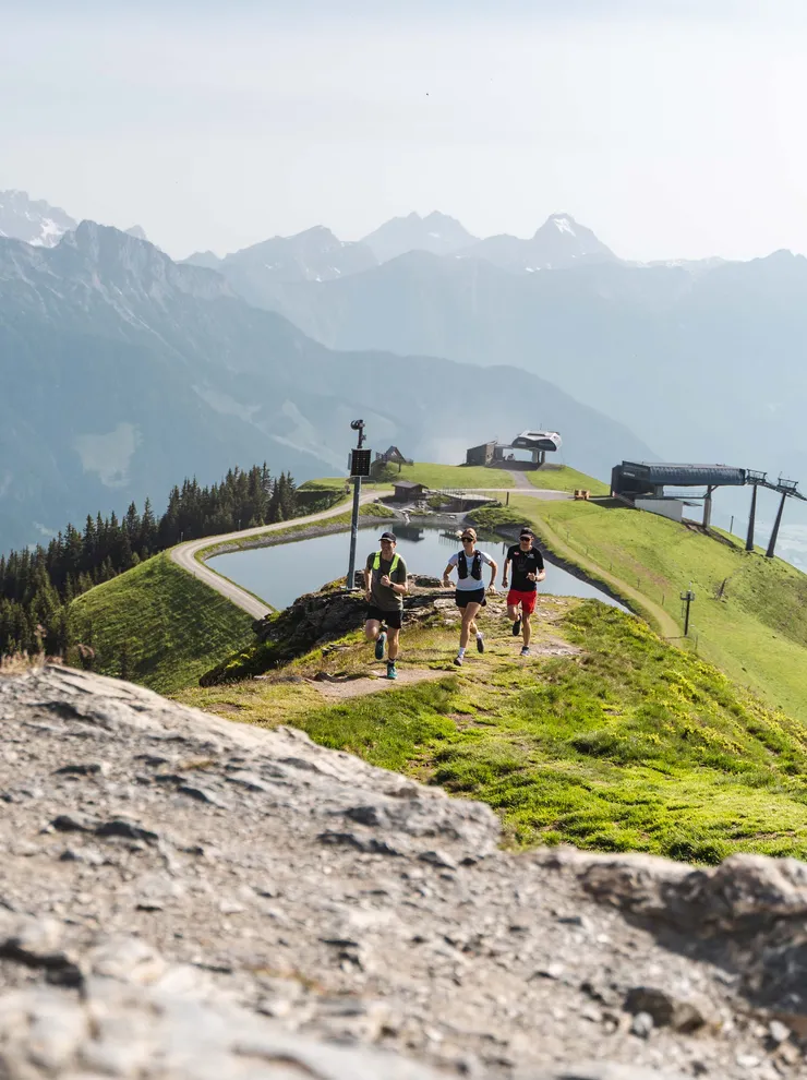Trail runners on a mountain ridge with alpine views and a cable car station