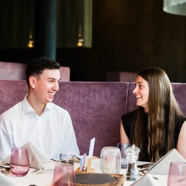 Lächelndes Paar sitzt an einem Tisch in modernem Restaurant mit violetten Sitzecken