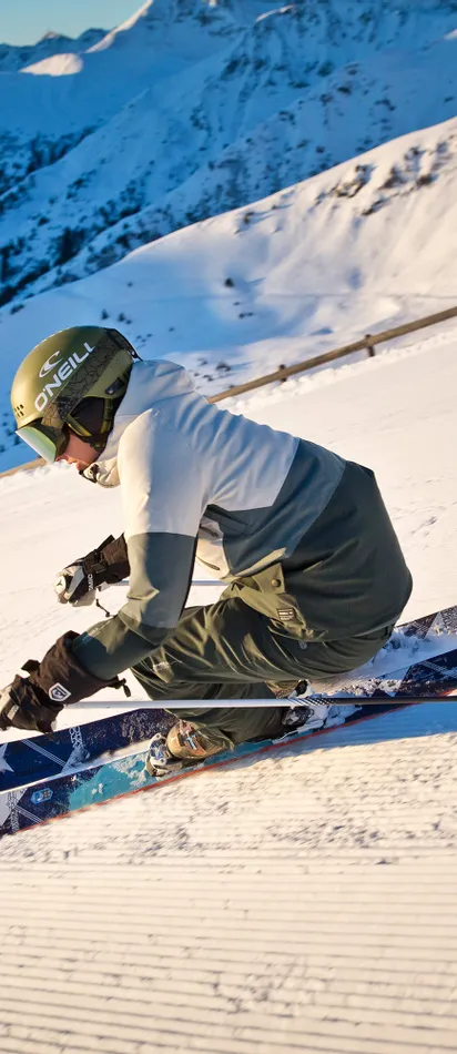 Skier carving on groomed slope with panoramic view of snow-covered alpine mountains