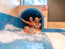 Familie lacht beim Verlassen einer Indoor-Wasserrutsche ins Becken