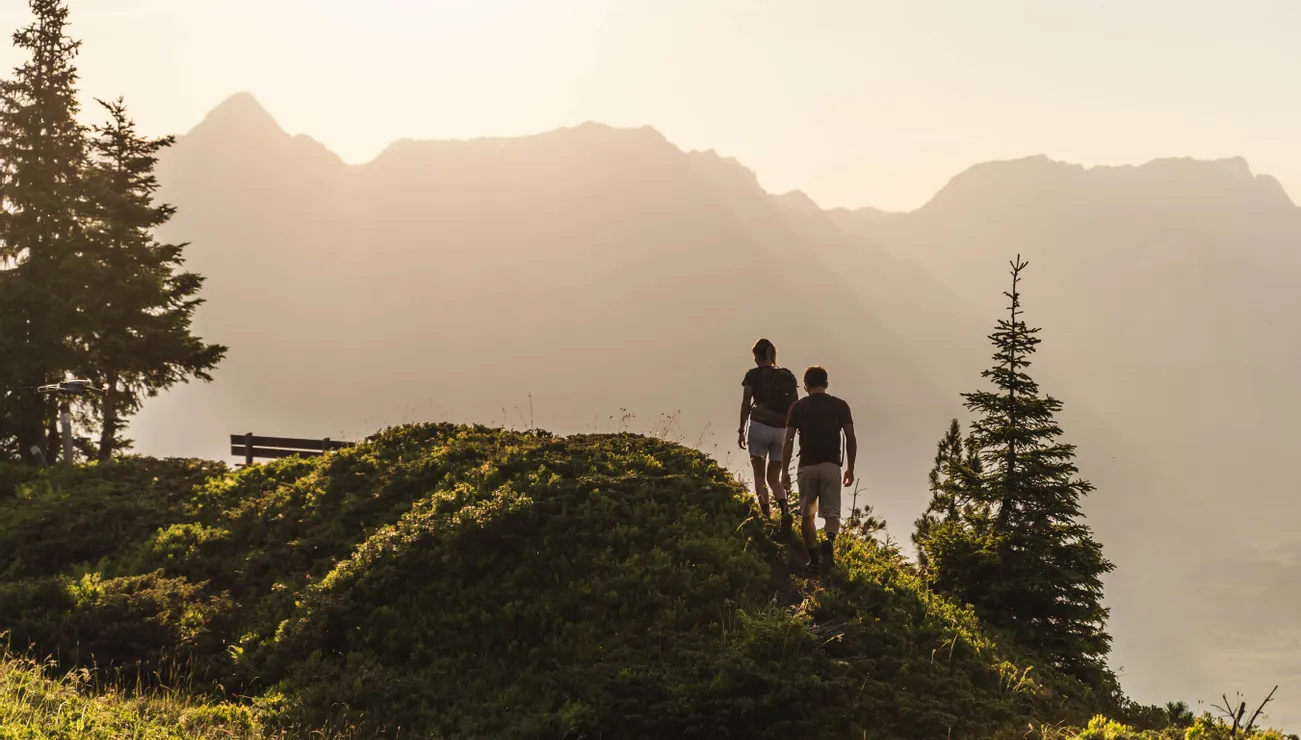 Paar wandert bei Sonnenuntergang auf einem Bergpfad mit Alpenpanorama