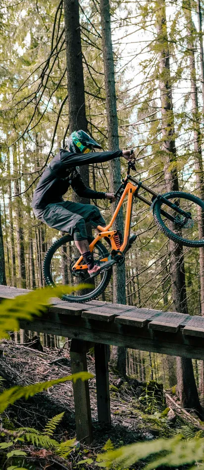 Mountain biker doing a wheelie on wooden trail ramp in forest
