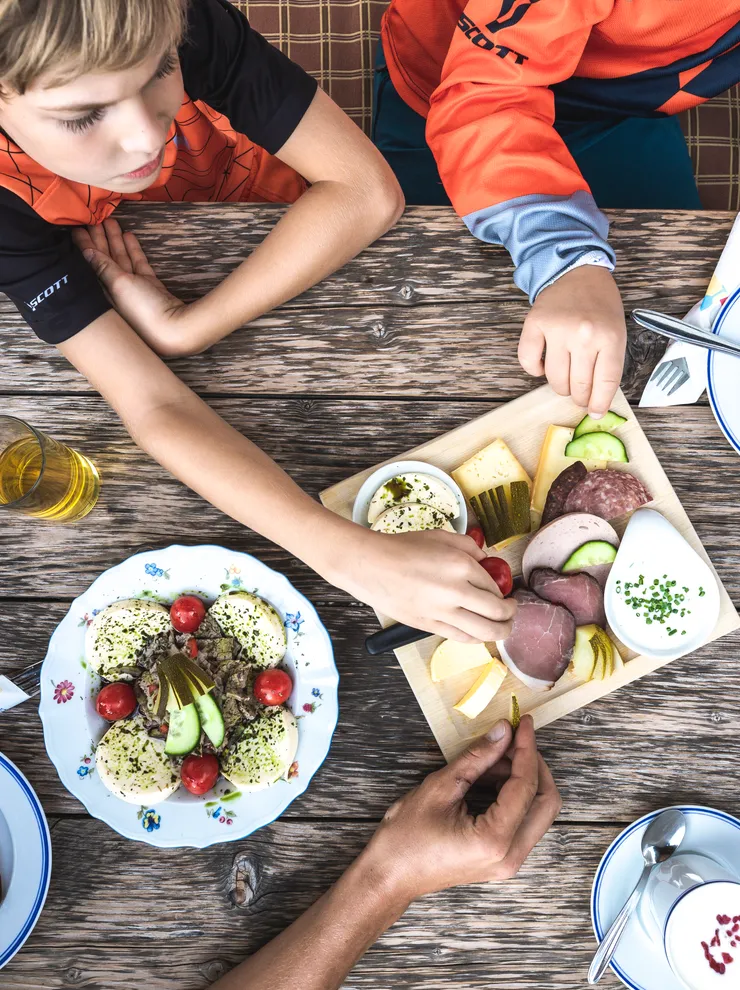 Kinder greifen nach einer traditionellen Jause mit Wurst, Käse und Brot auf Holztisch
