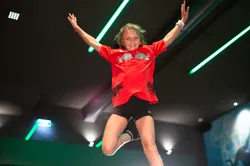 Kind springt mit ausgebreiteten Armen auf Indoor-Trampolin in moderner Trampolinhalle