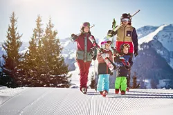 Family walking with skis on snowy slope in alpine ski resort on sunny winter day