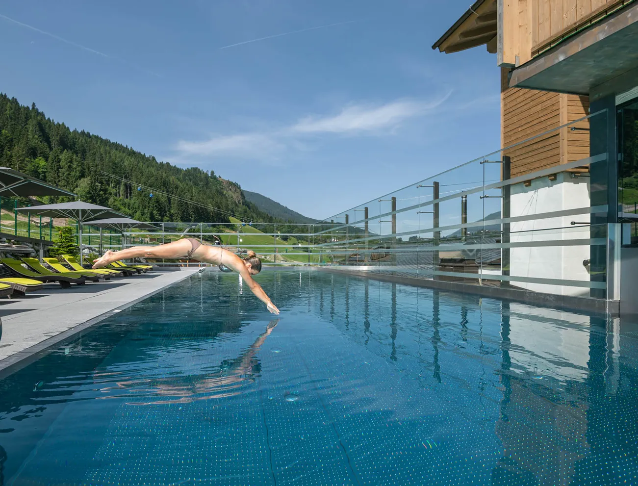 Frau springt in Infinity-Pool im Berghotel bei sonnigem Wetter