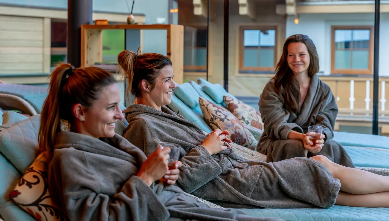 Women in bathrobes relaxing on lounge chairs with drinks at a luxury spa