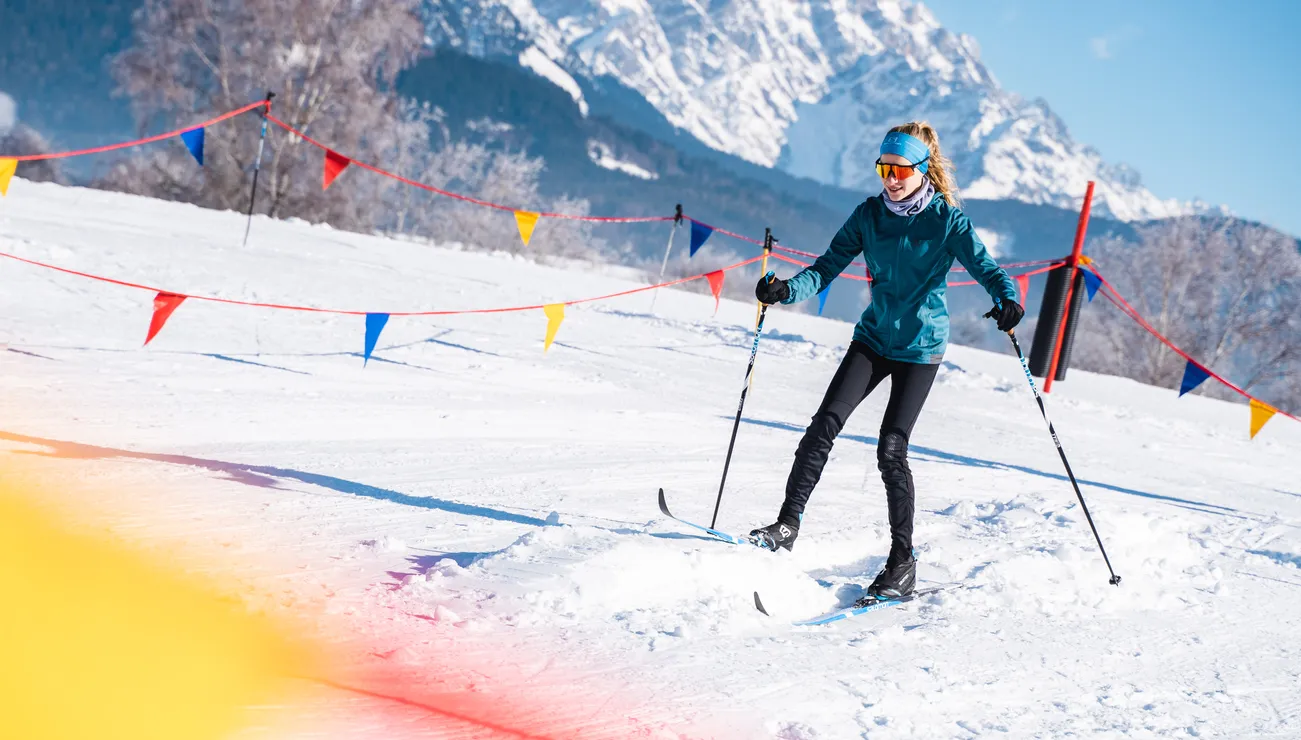 Frau beim Langlaufen auf verschneiter Strecke mit Alpen im Hintergrund