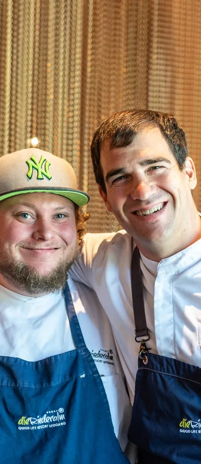 Two smiling chefs in uniforms and aprons posing together in a restaurant