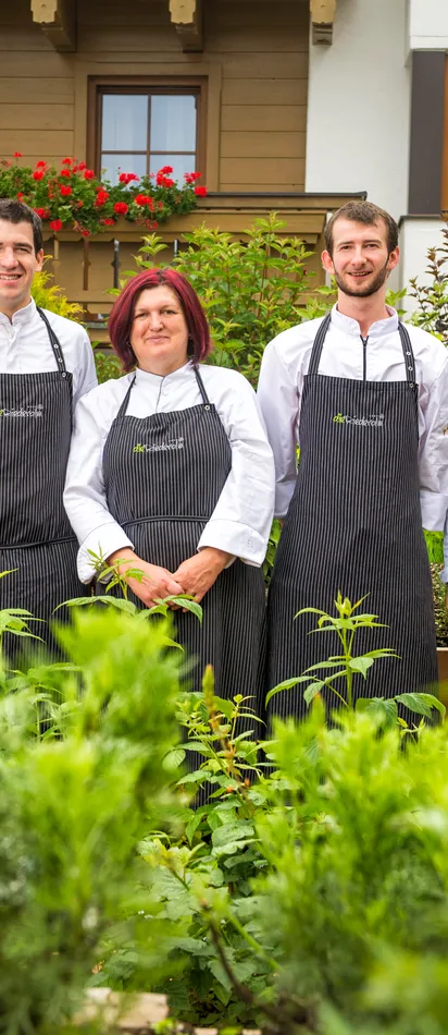 Team of chefs in striped aprons standing in herb garden in front of alpine-style restaurant