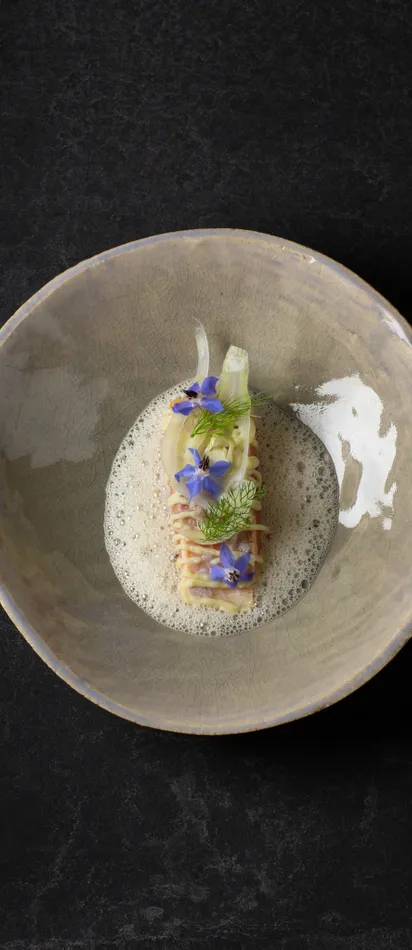 Gourmet-Pastagericht mit Schaum, Fenchel und essbaren blauen Blüten in Keramikschale