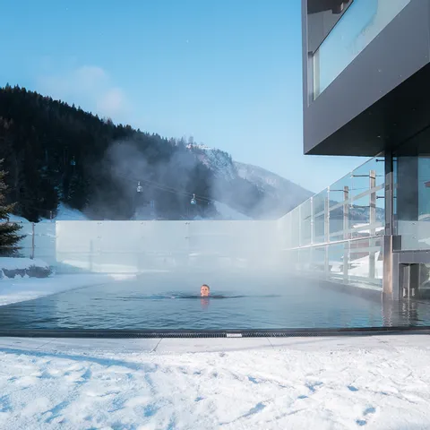 Outdoor heated pool with swimmer at modern hotel in snowy mountain landscape