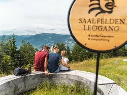 Familie auf Holzbank mit Blick auf die Berge in Saalfelden Leogang beim Wandern