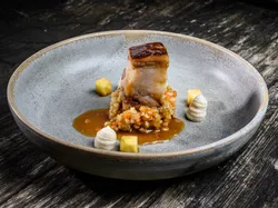 Gourmetgericht mit Schweinebauch, Gemüseperlen und Püreekunst auf Keramikteller