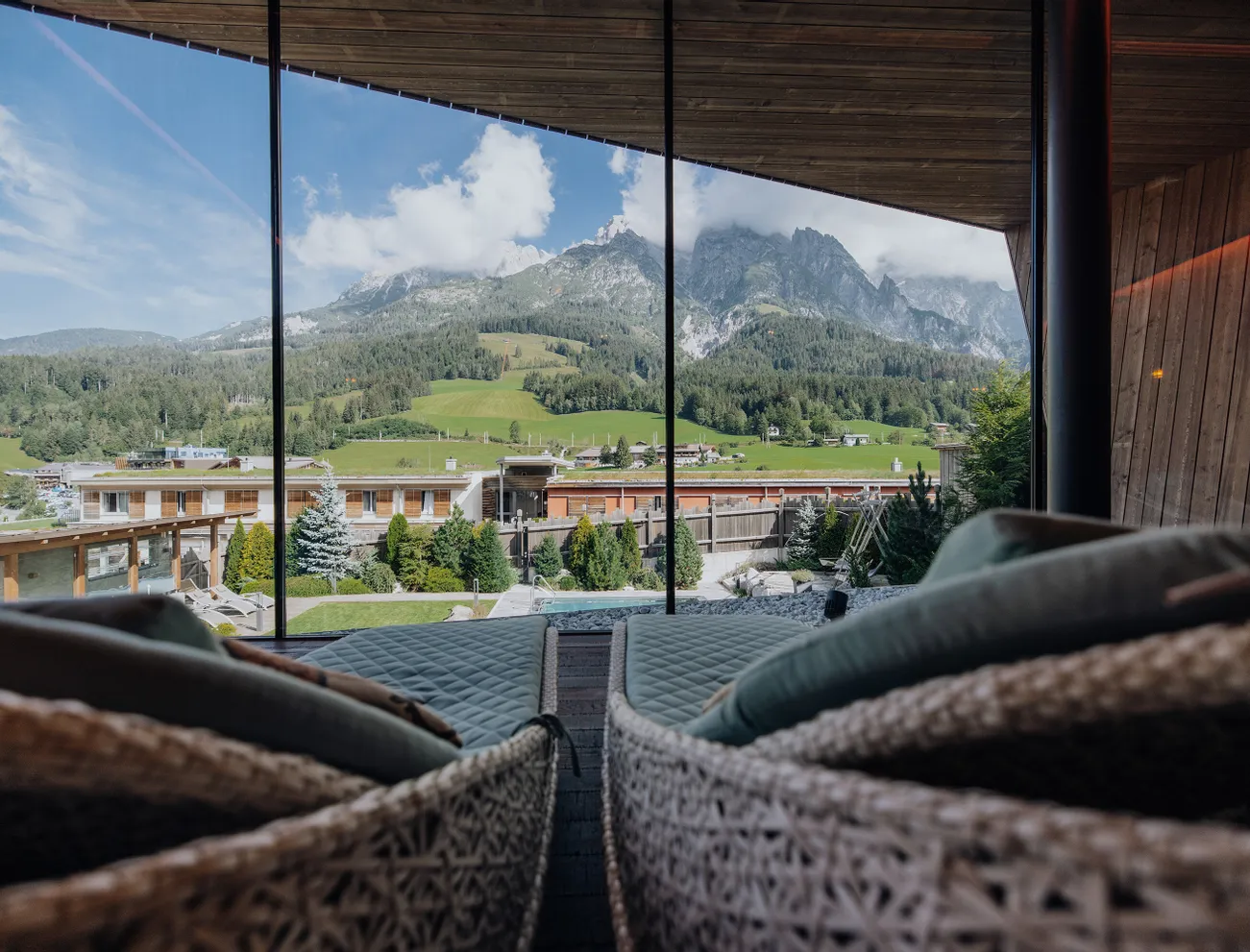 Panoramablick auf Alpenhotel, grüne Hügel und Berge durch Glasfront vom Spa-Ruheraum