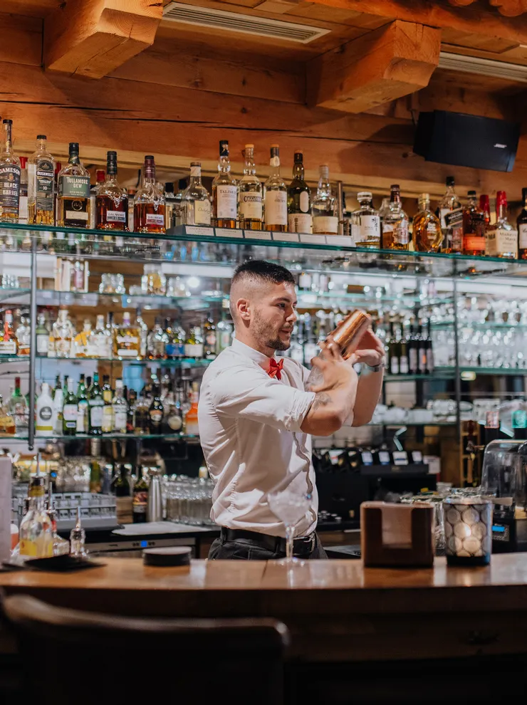 Bartender shaking cocktail at wooden bar with liquor bottles in background