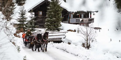 Pferdeschlitten auf verschneitem Weg vor Berghütte im Winter mit Solarpanel