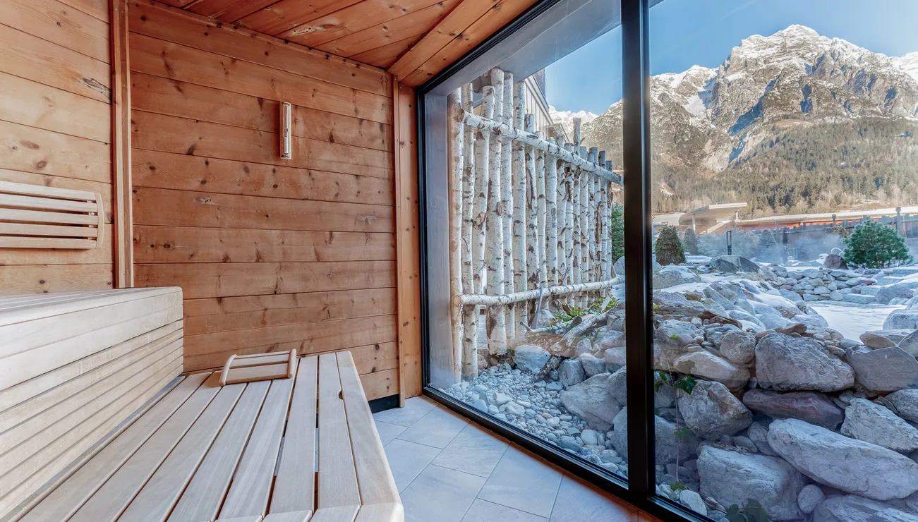 Holzsauna mit Panoramafenster und Blick auf schneebedeckte Alpenberge