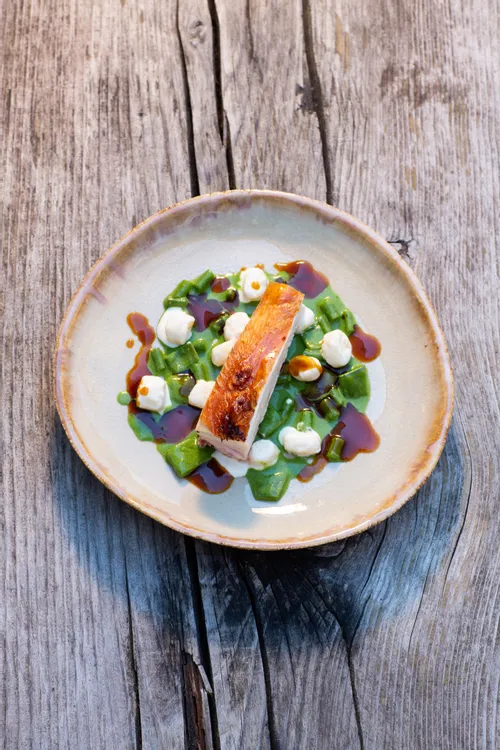 Gourmet roasted chicken breast served with green pasta, sauce drops and cream on rustic plate