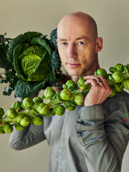 Mann trägt einen Strunk Rosenkohl und frischen grünen Kohl über der Schulter