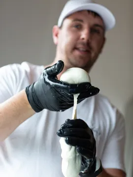 Man stretching fresh mozzarella cheese by hand wearing black gloves