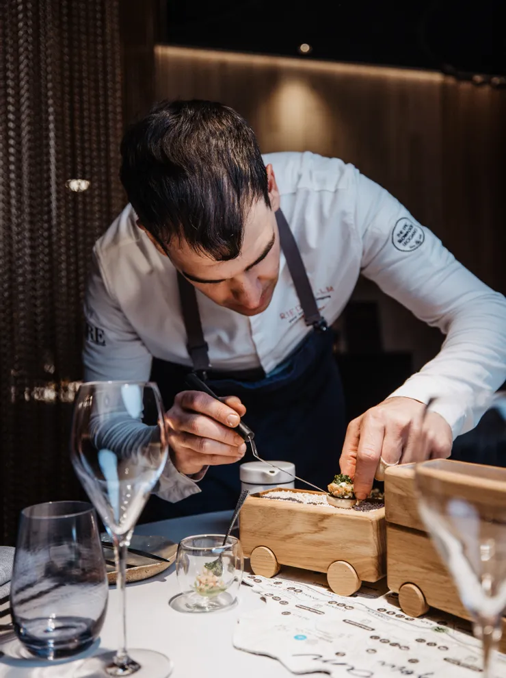 Chef plating gourmet dish on wooden serving cart in fine dining restaurant