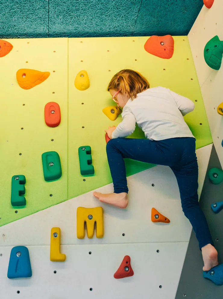Kind klettert an Indoor-Boulderwand mit bunten Griffen in Buchstabenform
