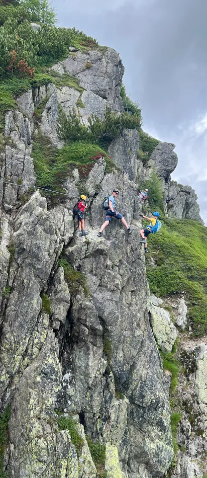 Gruppe von Kletterern an einer felsigen Bergwand mit Sicherheitsgurten unter bewölktem Himmel