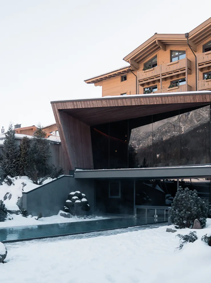 Modern alpine hotel with outdoor pool surrounded by snow in a winter landscape