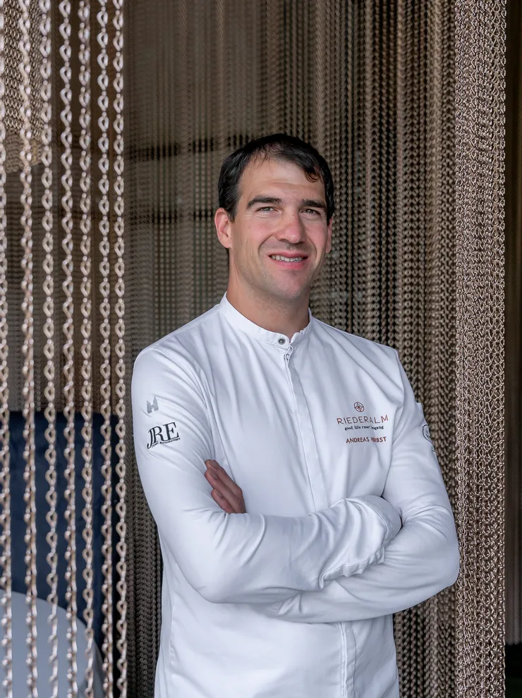 Koch in weißer Riederalm-Uniform vor dekorativem Kettenvorhang