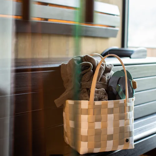 Woven basket with towels and flip-flops on a wooden sauna bench