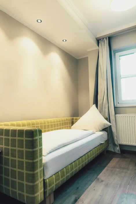 Kleines modernes Gästezimmer mit grünem Karo-Tagesbett, weißer Bettwäsche und sanfter Beleuchtung