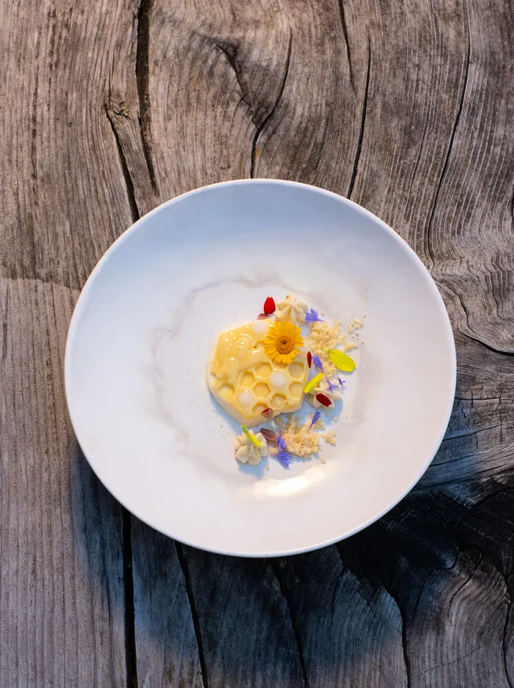 Gourmet-Dessert mit Wabenstruktur und essbaren Blüten auf weißem Teller auf rustikalem Holztisch